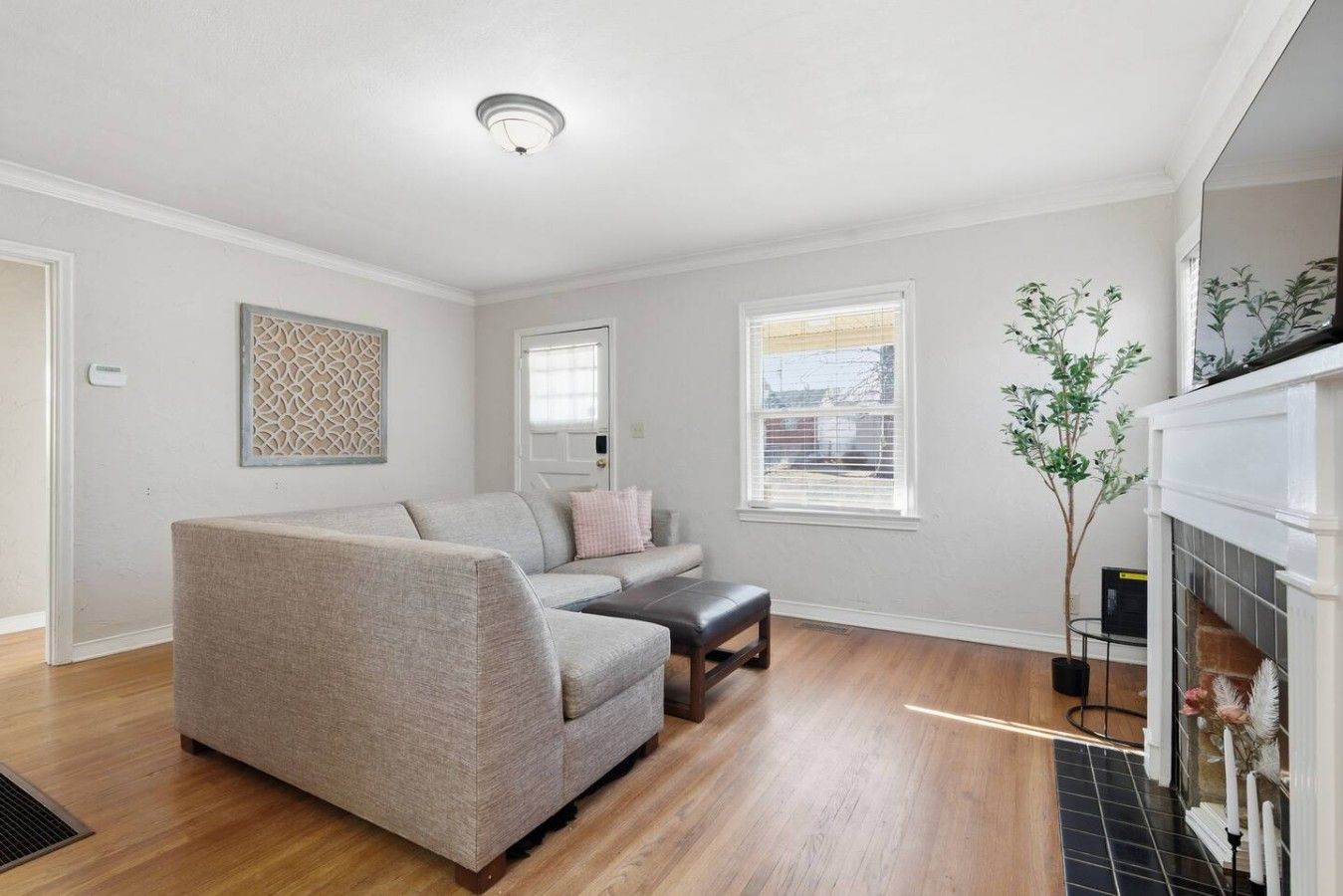 A living room with a grey sofa, a small table, a fireplace, and a window with blinds.