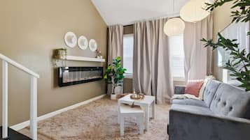 A living room with a fireplace, a grey sofa, a white coffee table, and a plant.