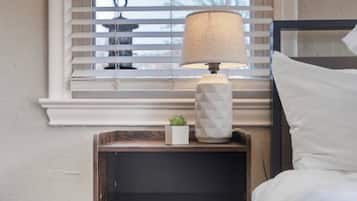 A bedroom with a bed, a bedside table with a lamp, and a window with blinds.