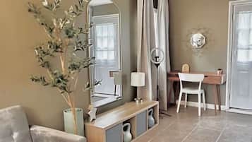 Un salon comprenant un canapé, un bureau, une chaise, un miroir, une plante et un radiateur.