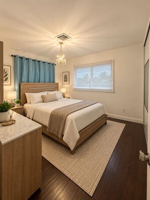 Ein Schlafzimmer mit einem Bett, Nachttischen, einem Schranken, einer Kandelaber, einem Fenster mit Jalousien und einer Tür.
