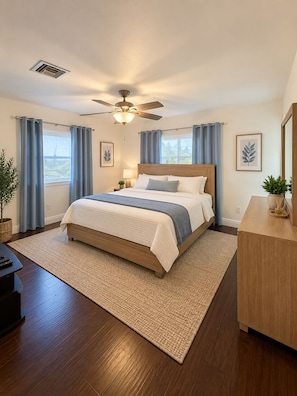 Une chambre à coucher comprenant un lit, un ventilateur de plafond, une table de chevet, une lampe, une plante en pot et une commode.