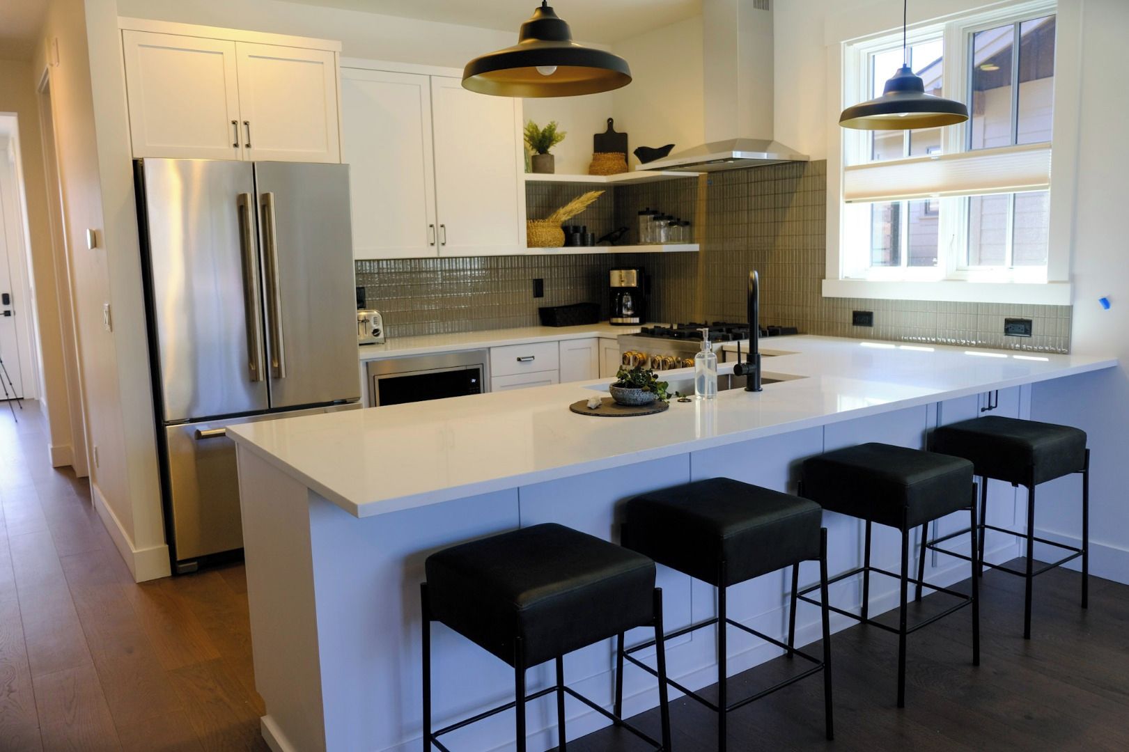 A modern kitchen with a large island, stainless steel appliances, and black bar stools.