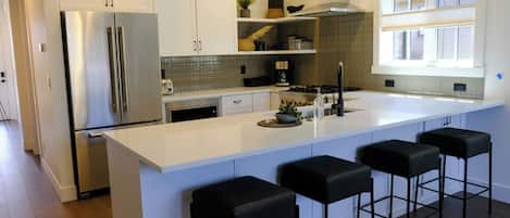 A modern kitchen with a large island, stainless steel appliances, and black bar stools.