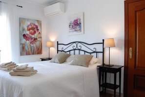 A hotel room with a bed, two bedside tables with lamps, a door, and two wall-mounted air conditioning units. - Apartment in Nerja Near Burriana Beach (Nerja)
