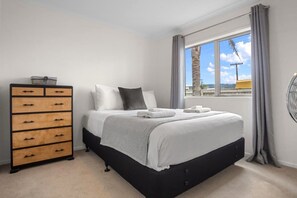A bedroom with a bed, a dresser, and a window with curtains. - Whanga on Foot - Brilliant Location (Whangamatā)