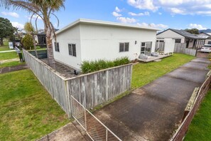 A single-story residential building with a flat roof, a front porch, and a fenced yard. - Whanga on Foot - Brilliant Location (Whangamatā)