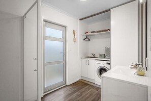 A compact laundry room with a washing machine, a sink, and storage cabinets. - Whanga on Foot - Brilliant Location (Whangamatā)