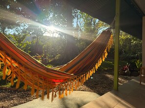Uma rede sob área sombreada, com vista para árvores e um jardim.
