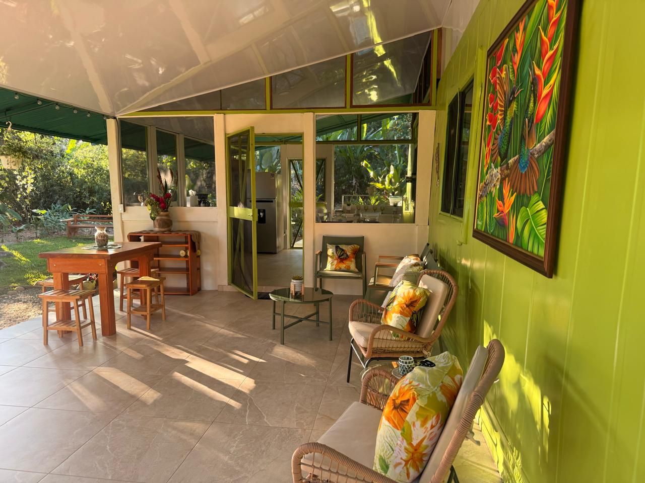 A covered patio area with a dining table and chairs, a sofa, and a painting on the wall.