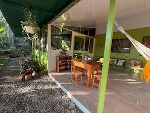Um espaço ao ar livre coberto com uma mesa e cadeiras de madeira, uma rede e vasos com plantas.