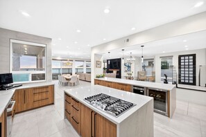 A modern kitchen with a central island, built-in appliances, and a dining area with a view. - Ocean Lane Luxury - 4B 4BA Private Elegance w Pool (Imperial Beach)