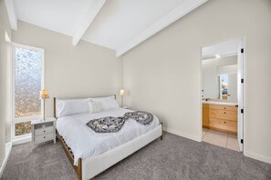 Ein Schlafzimmer mit Bett, Nachttischen, einem Fenster mit Milchglas und einem Badezimmer mit Spiegel und Waschbecken.