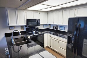 A kitchen with white cabinets, a black refrigerator, a microwave, and a kettle. - Spectacular Ocean Front Condo! Watch for Whales! Whaler at Depoe Bay! (Depoe Bay)