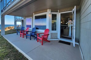 A covered outdoor seating area with Adirondack chairs, a view of the ocean, and a door leading to an interior space. - Spectacular Ocean Front Condo! Watch for Whales! Whaler at Depoe Bay! (Depoe Bay)