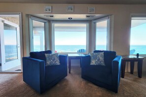 A room with a view of the ocean, featuring two blue armchairs with patterned cushions, a small table, and a ceiling vent. - Spectacular Ocean Front Condo! Watch for Whales! Whaler at Depoe Bay! (Depoe Bay)