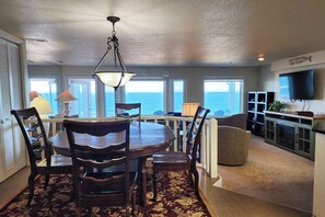 A dining area with a round table, chairs, and a chandelier. There is a view of the ocean through large windows. - Spectacular Ocean Front Condo! Watch for Whales! Whaler at Depoe Bay! (Depoe Bay)