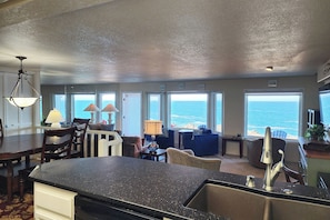 Cozinha com ilha grande, sala de jantar com cadeiras e vista para o oceano através de amplas janelas.