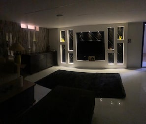 Ein modernes Wohnzimmer mit Flachbildfernseher, Einbauschränken und einem dunklen Teppich.