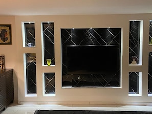 A living room with a large flat-screen TV mounted on a wall with decorative glass panels. - Enjoyable 2-bedroom apartment with AC in vibrant Amman (Amman)
