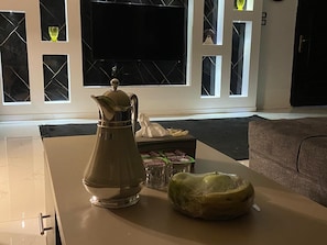 Ein Wohnzimmer mit Couchtisch, dekorativer Krug und verpacktem Geschenk, mit großem Fenster und Flachbildfernseher im Hintergrund.