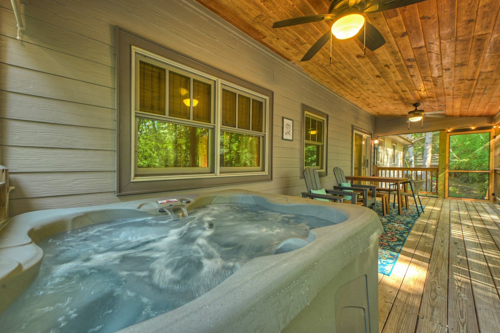 A hot tub area with a wooden deck, large windows, and ceiling fans.