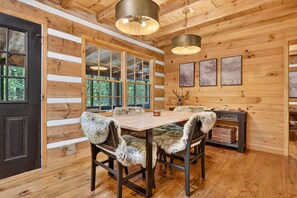 Ein Holzinterieur mit einem Esstisch, Stühlen mit Felldecken, einer Hirschdekoration und gerahmten Kunstwerken an der Wand.