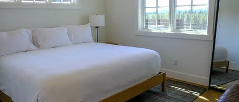 Un dormitorio con cama, mesita de noche, lámpara, ventana con vistas y espejo.