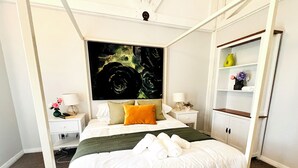 Un letto a baldacchino con biancheria bianca, un comodino con una lampada e una mensola a muro con oggetti decorativi.
