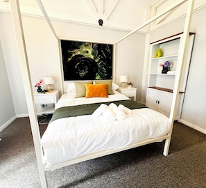 A four-poster bed with white bedding, a nightstand with a lamp, and a wall-mounted shelf with decorative items. - McLaren Vale Vineyard Loft | Full Kitchen + Bath (Blewitt Springs)
