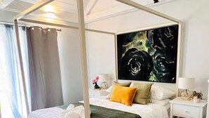 Un letto a baldacchino con copripiumino verde scuro, biancheria da letto bianca e un solo cuscino giallo. Sopra il letto, un'ampia pittura astratta.