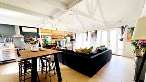 Un'ampia zona giorno con un divano scuro, un tavolo da pranzo in legno con sgabelli e una cucina sullo sfondo.