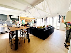 A spacious living area with a dark-colored sofa, a wooden dining table with stools, and a kitchen in the background. - McLaren Vale Vineyard Loft | Full Kitchen + Bath (Blewitt Springs)