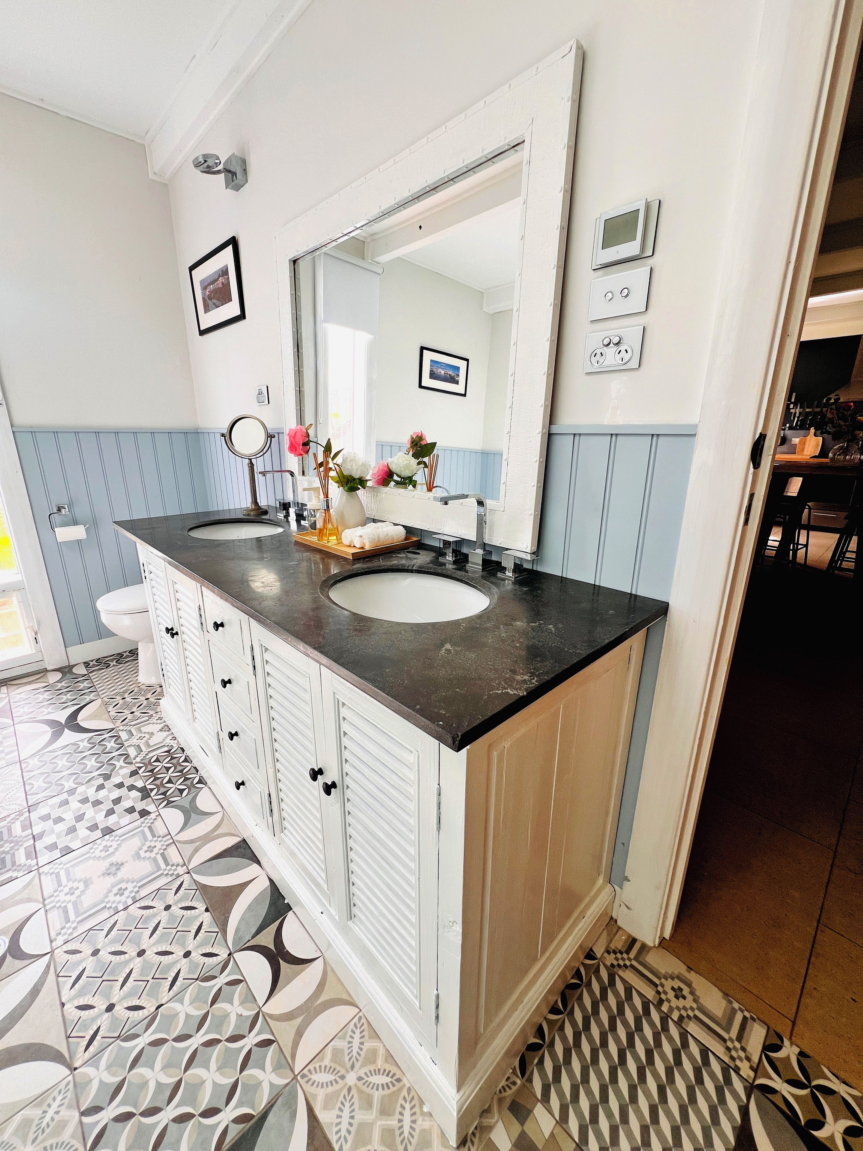 A bathroom with a large mirror, a sink, and a patterned floor.