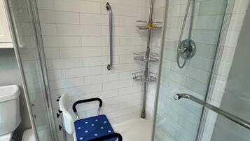 A shower area with a glass door, a white tiled wall, a blue wheelchair-accessible bench, and a handheld showerhead.