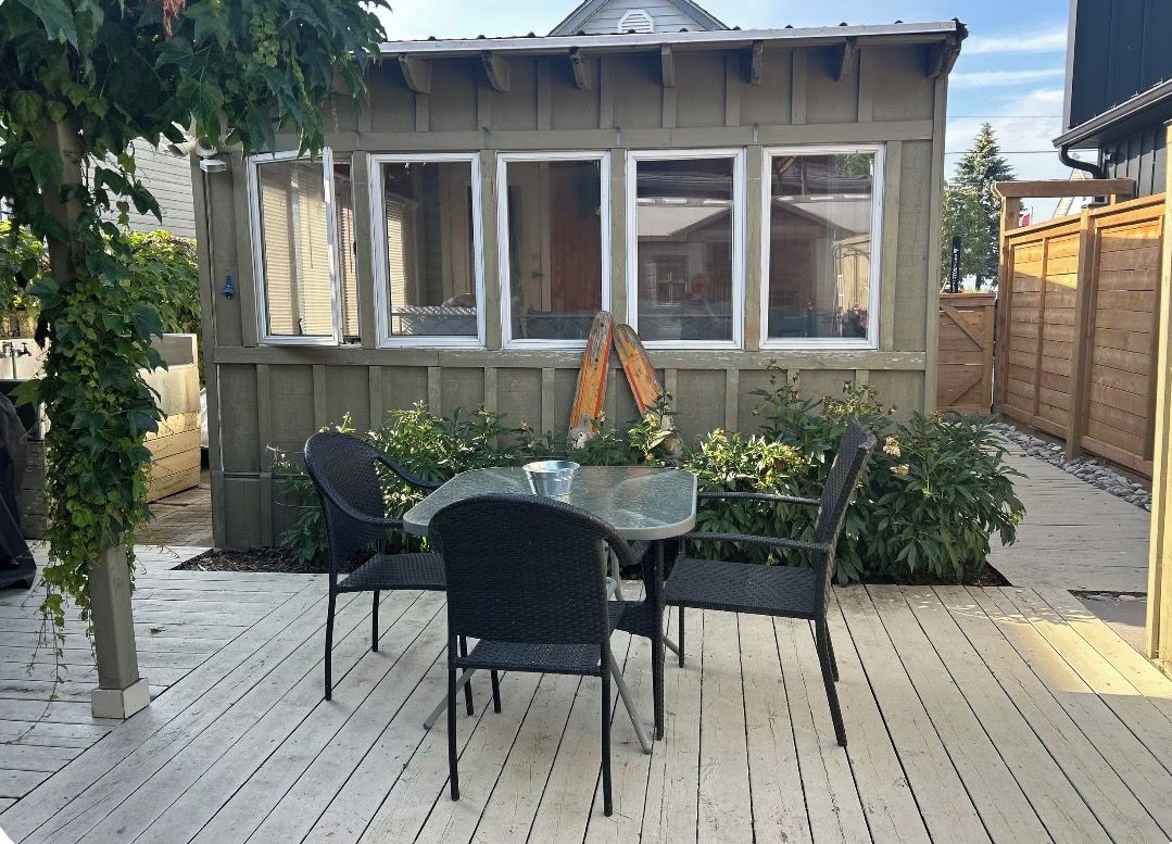 Une terrasse en bois avec une table et des chaises en verre, entourée de plantes et d’une clôture en bois.
