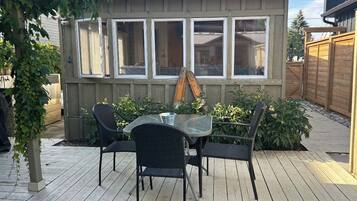 Une terrasse en bois avec une table et des chaises en verre, entourée de plantes et d’une clôture en bois.