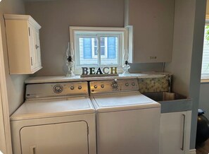 Een wasruimte met een wasmachine, droger en een raam met de tekst 'BEACH'.