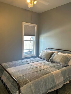 A bedroom with a bed, a window with blinds, and a ceiling light fixture.