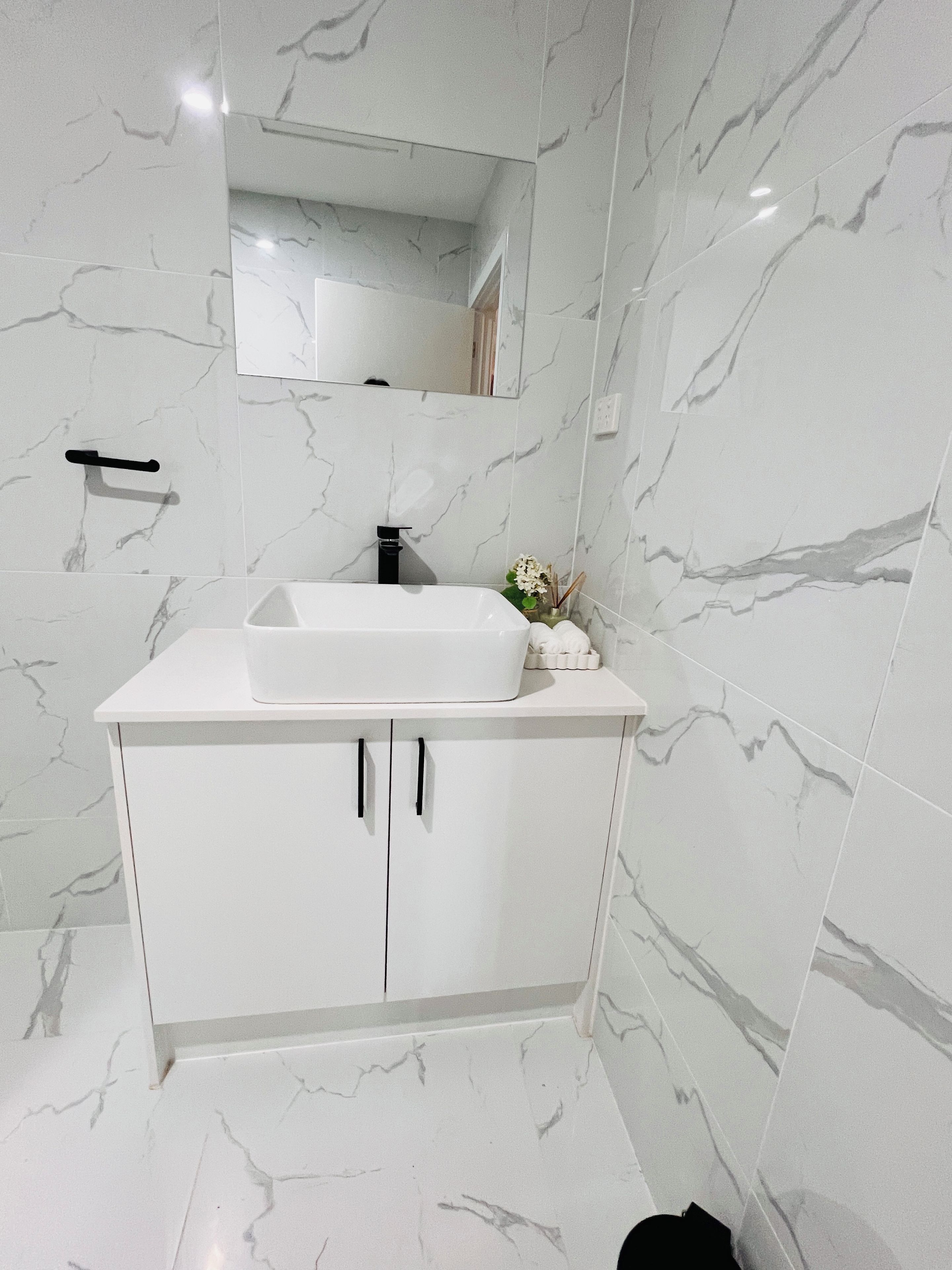 A bathroom with a white vanity, a mirror above the sink, and marble-patterned walls.