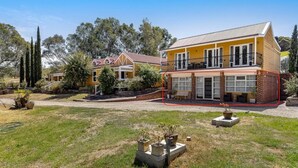Uma casa amarela de dois andares com varanda, cercada por um gramado e árvores.