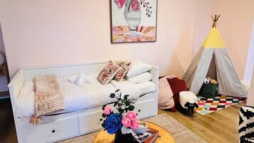A cozy living room with a sofa, a round wooden coffee table with a vase of flowers, a colorful rug, and a teepee tent.