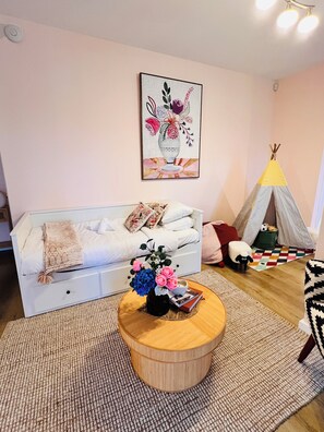 Een gezellige woonkamer met een bank, een rond houten bijzettafeltje met een bloevas, een kleurrijk vloerkleed en een tipi tent.