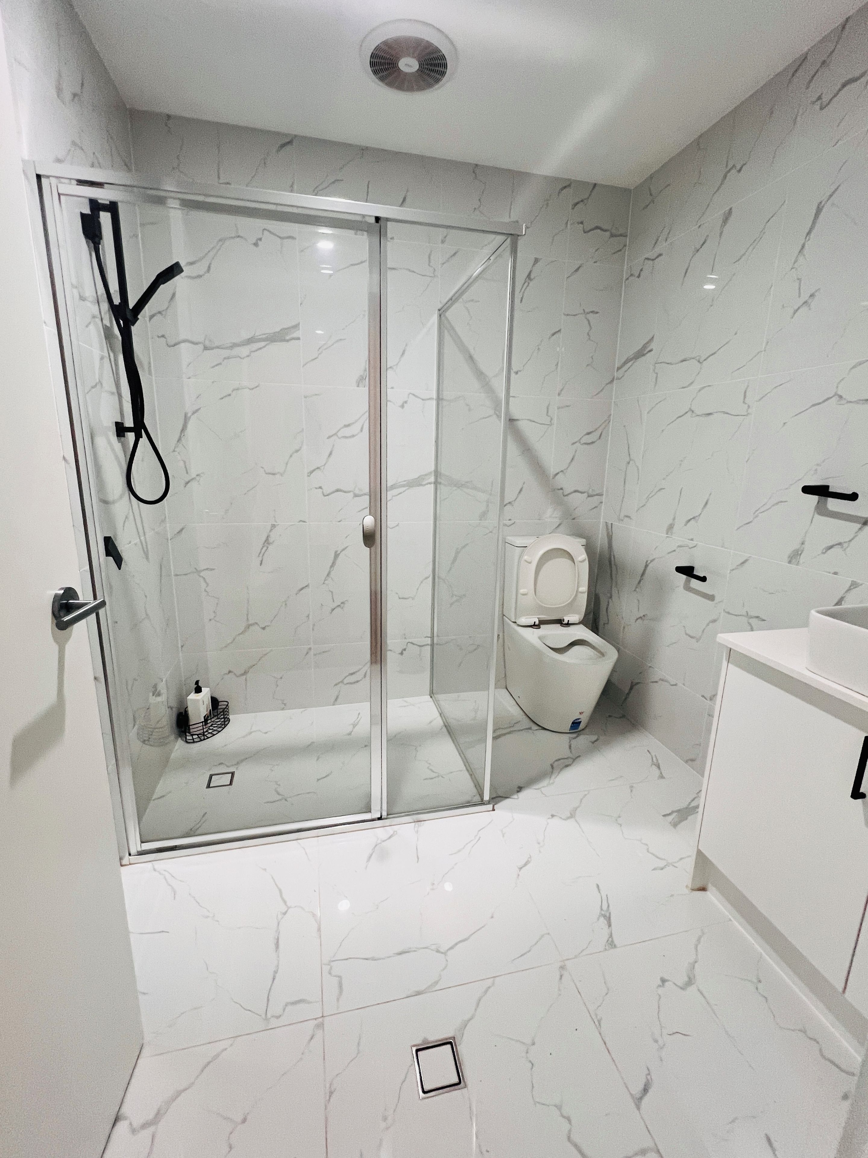 A bathroom with a glass-enclosed shower, a toilet, and a sink.