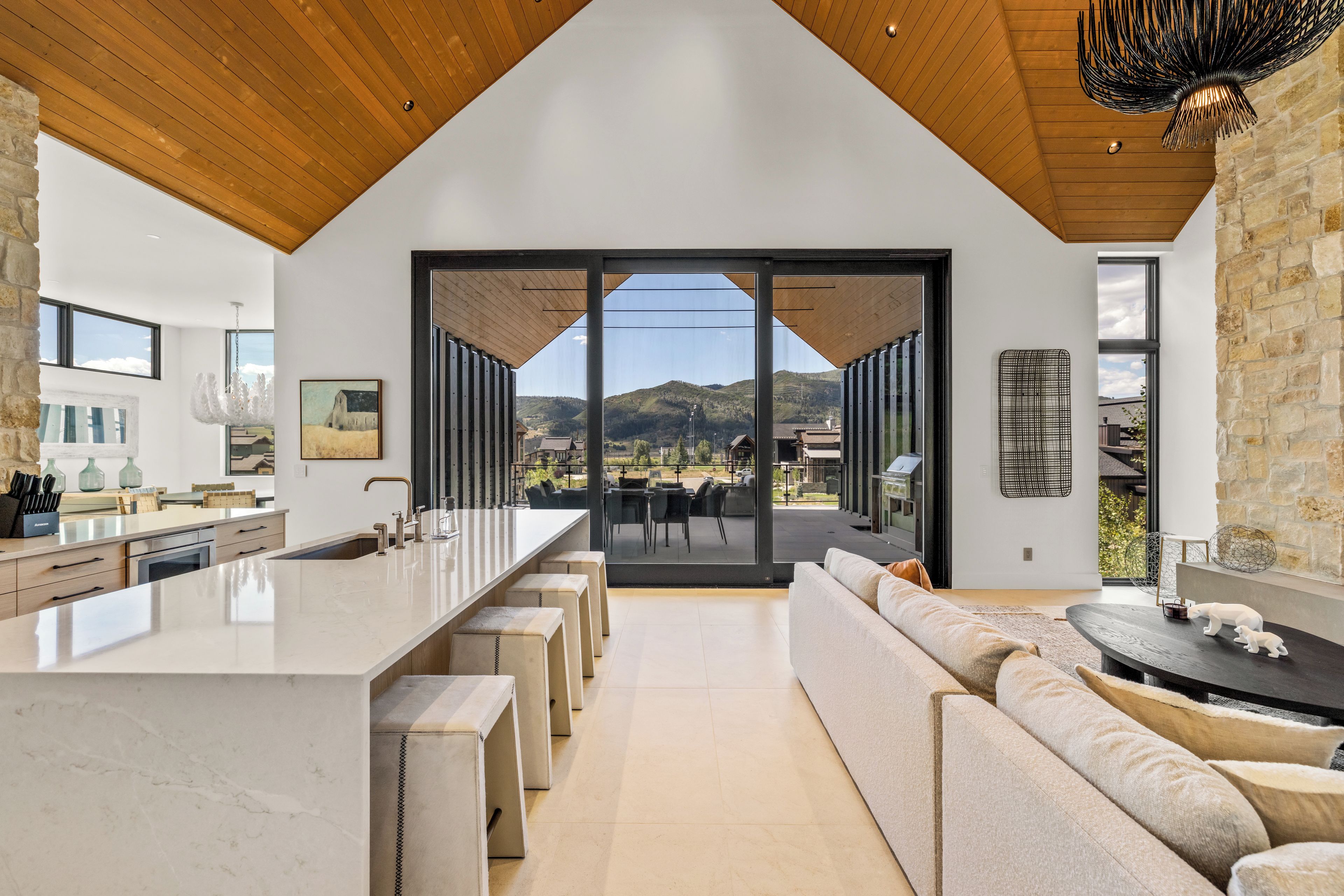 A modern kitchen with a large island, a dining area with a view, and a stone accent wall.