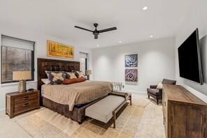 A modern bedroom with a large bed, a ceiling fan, a flat-screen TV, and artwork on the walls. - French Point Ridge! Elegant, Brand New Single Family Home, Amazing! (Steamboat Springs)
