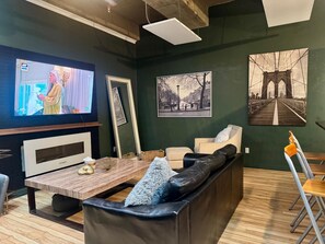 A living room with a TV, a sofa, a coffee table, and framed pictures on the wall. - Cambridge Loft on Jasper Ave \| ICE District (Edmonton)