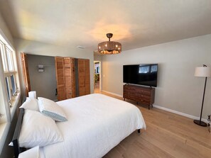 A bedroom with a large bed, wooden wardrobe, a television, and a floor lamp. - Cypress Cove - Private Canal Front Retreat in Sugarloaf (Sugarloaf Key)