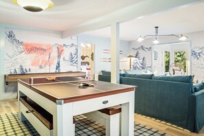 A room with a ping pong table, a sofa, and a wall with a mountain design. - Wild & Well - Red Light • Sauna • Gym • Hot Tub (McGaheysville)
