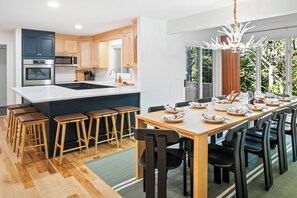 A modern kitchen with a central island, bar stools, and a dining area set for six. - Wild & Well - Red Light • Sauna • Gym • Hot Tub (McGaheysville)